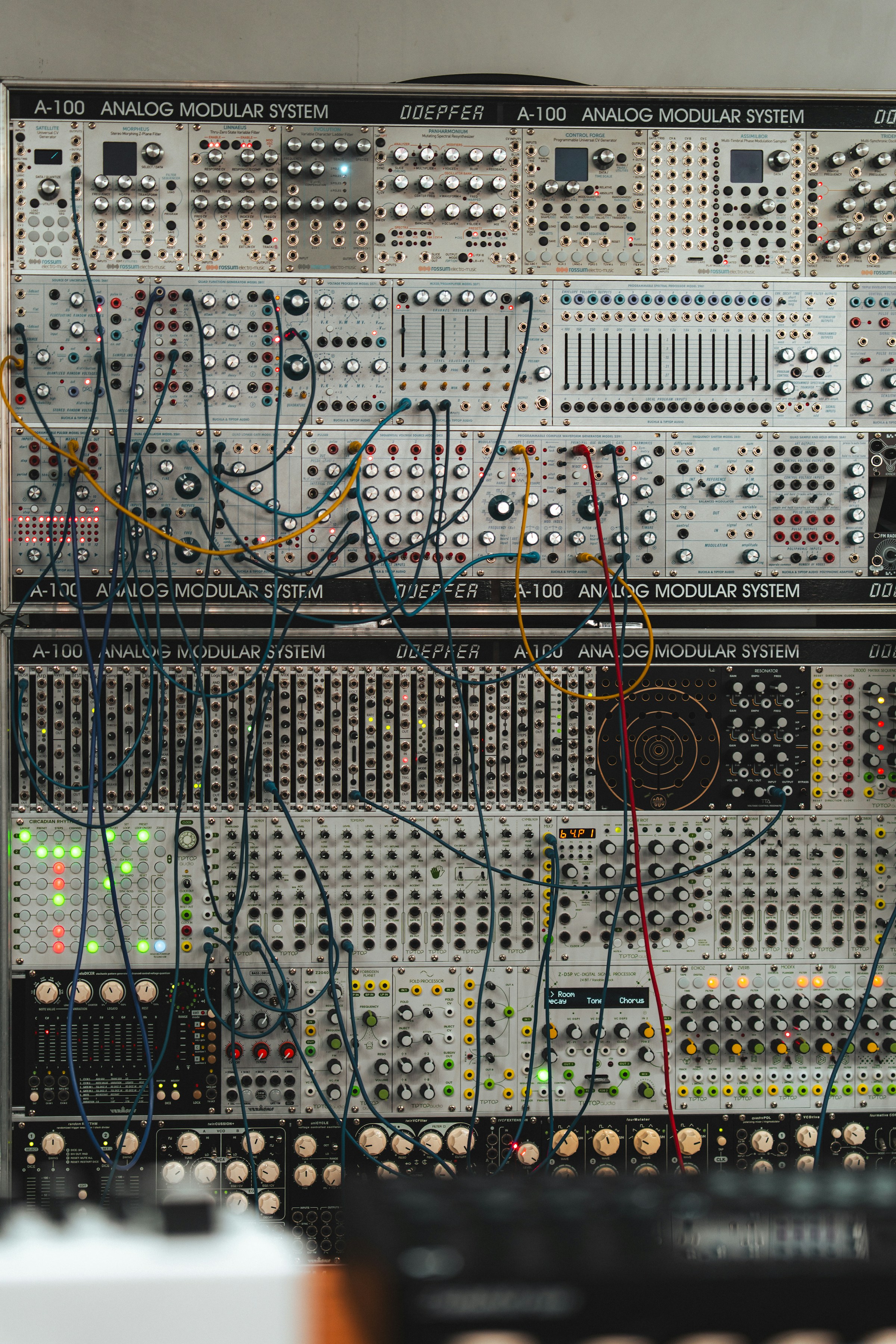 A Doepfer modular synthesizer rack with yellow, teal and red patch cables plugged between the modules