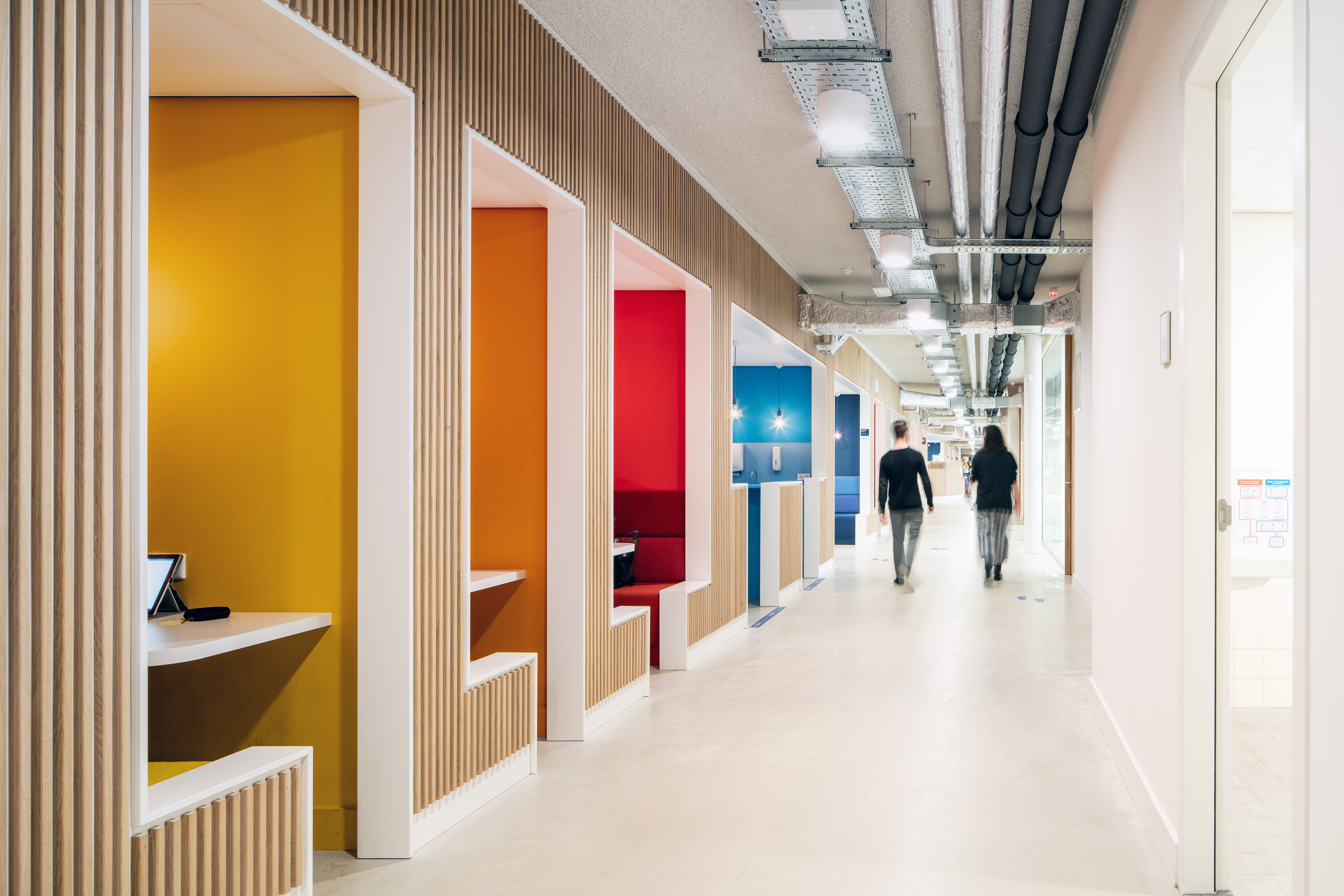 A corridor at Tapijn with yellow, orange, red and blue study alcoves in timber frames