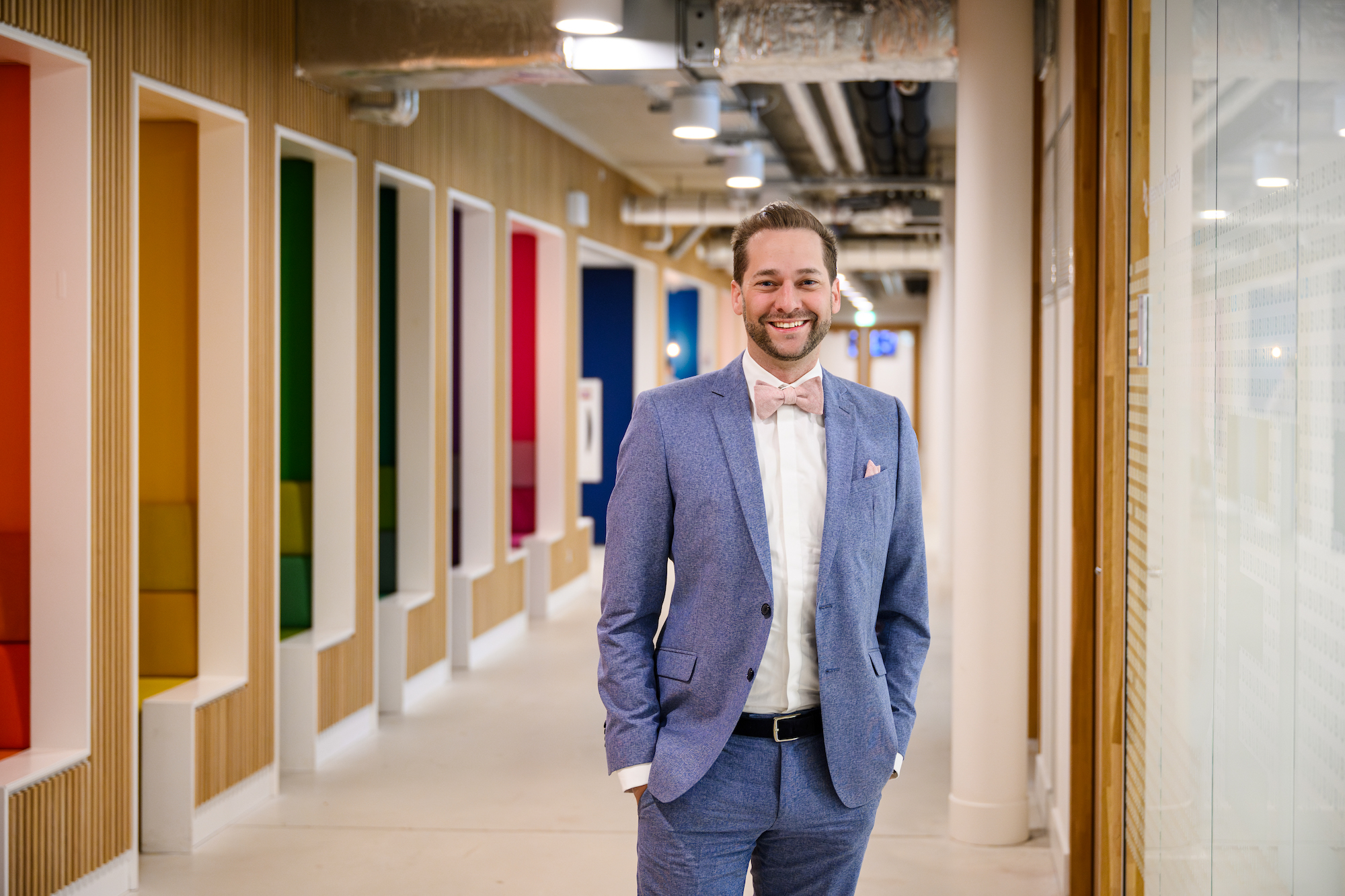 Jermain Kaminski in a bright university corridor at Maastricht University, in a blue blazer and pink bow tie